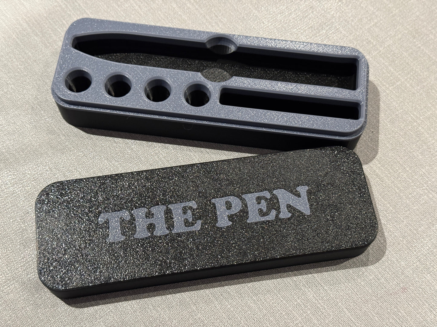Black and grey KwikPen case with 'THE PEN' engraving in a grey on black background
